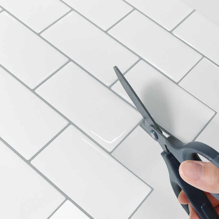 Person using scissors to cut a white tile