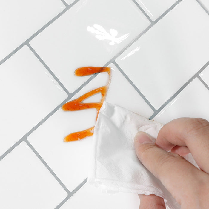 Hand using a white cloth to wipe up a small amount of orange liquid on a tiled surface.