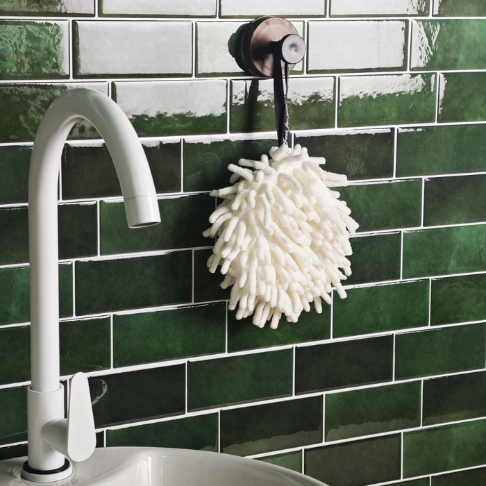 White scrubber hanging from a faucet against a green tiled wall