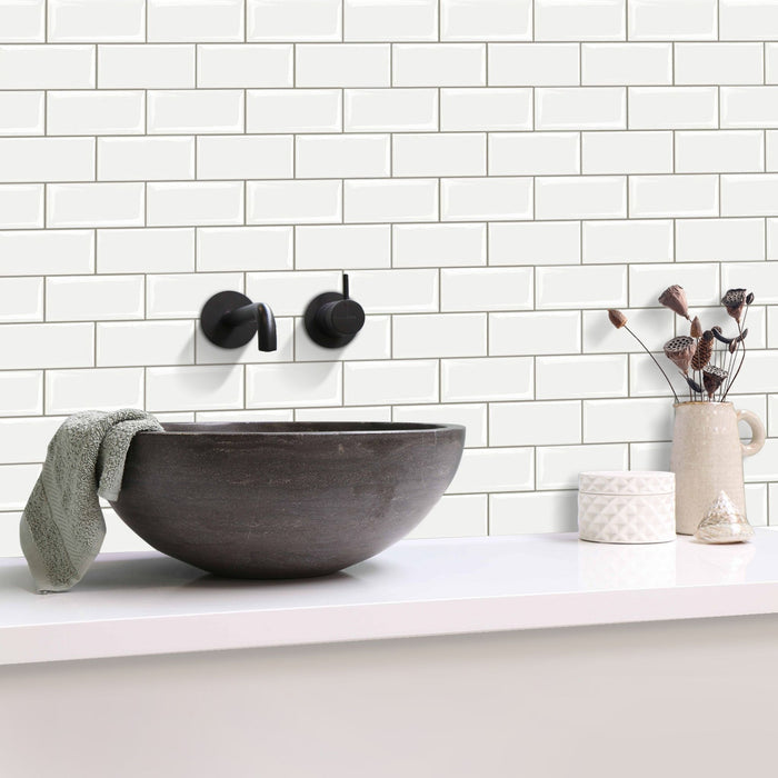 White subway tile backsplash on a bathroom wall with a dark charcoal vessel sink, matte black wall-mounted faucet, white countertop, and small decorative ceramic items.