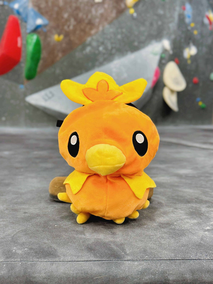 Handmade orange plush Torchic fire chick climbing chalk bag for bouldering. Features yellow feather tufts and a cute bird silhouette. High-quality plush bouldering gift with a 12cm reinforced rim, secure drawstring, and deep black fleece lining for rock climbing.