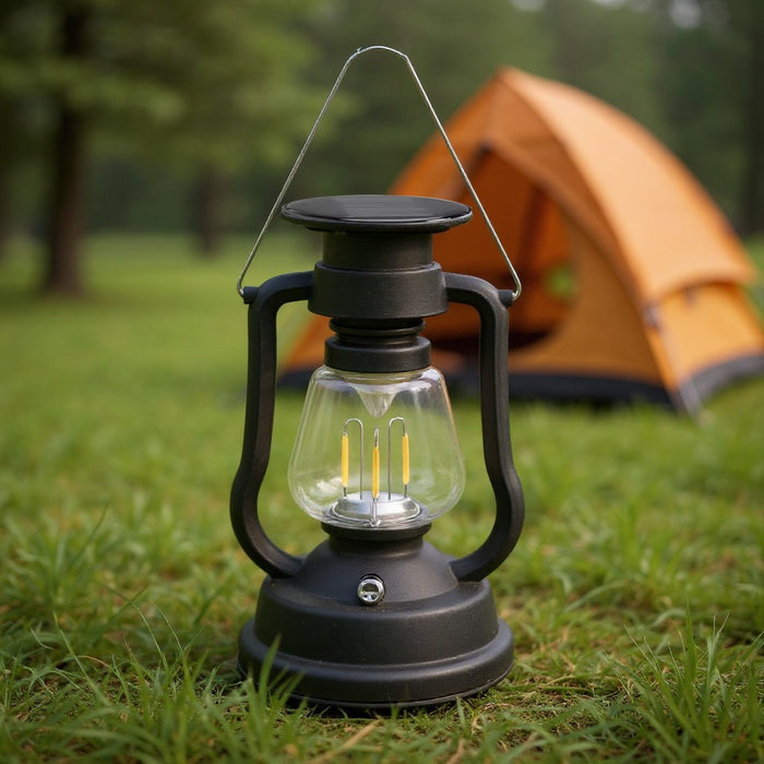 Black vintage-style LED lantern placed on grass with an orange camping tent in the background.