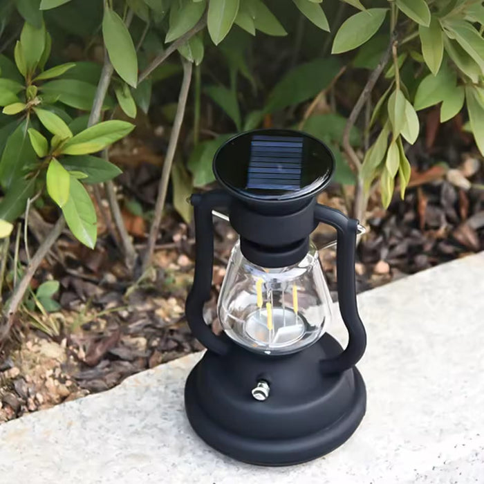 Solar-powered lantern placed on the ground near green foliage.