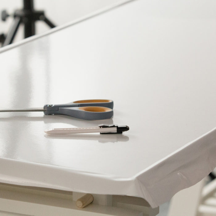 A panel being covered with white glossy adhesive vinyl with grey scissors and a white craft knife on top.