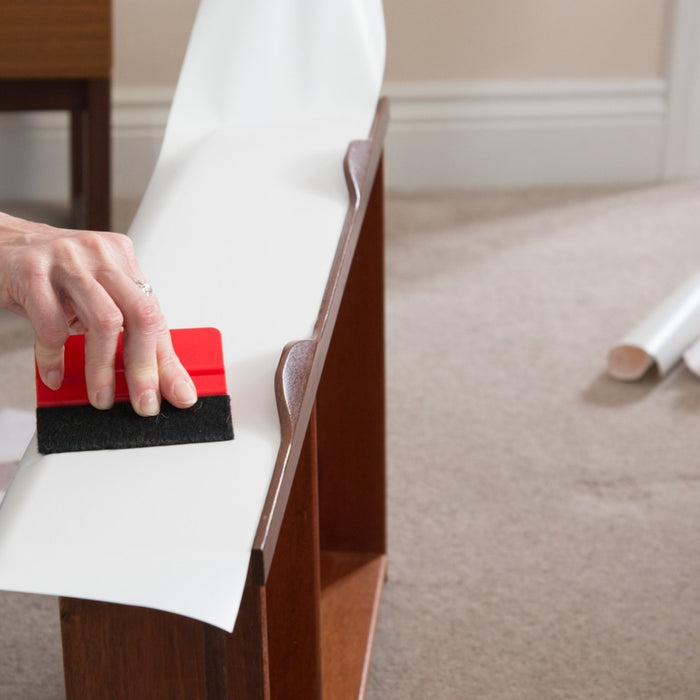 White matte adhesive vinyl being installed on a drawer front. A and holding a ed squeegee with a black felt tip