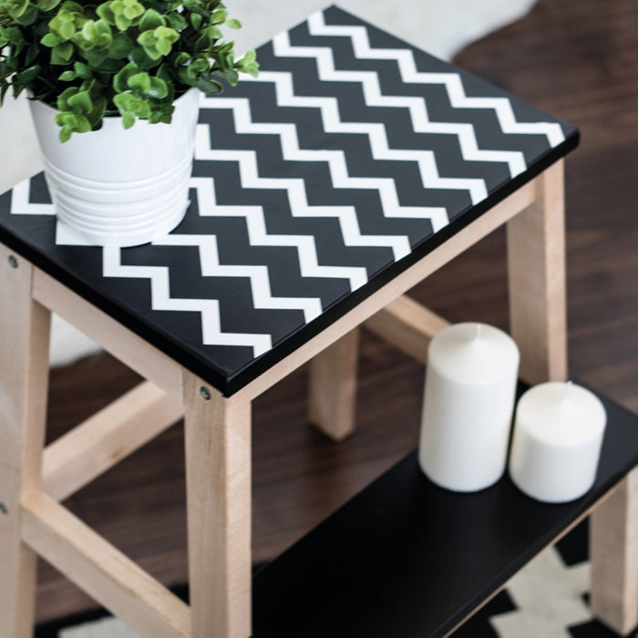 A step stool covered with black adhesive vinyl and white matte vinyl in a zig zag pattern.